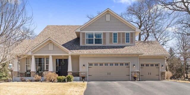 craftsman house with a shingled roof, covered porch, stone siding, and aphalt driveway