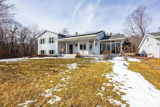 view of front of home featuring covered porch, solar panels, a chimney, and a sunroom