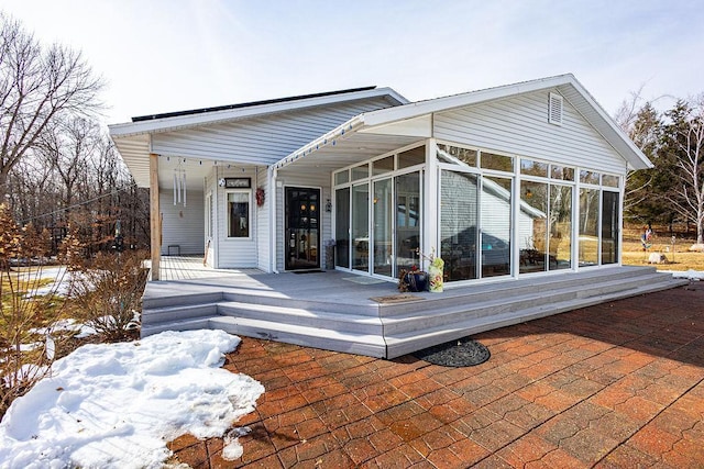 snow covered house featuring a sunroom