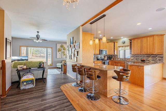 kitchen with tasteful backsplash, light stone counters, appliances with stainless steel finishes, a peninsula, and wood finished floors