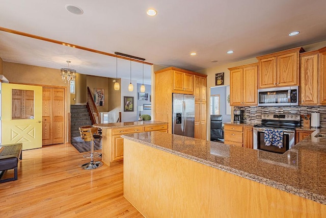 kitchen featuring light wood-type flooring, a peninsula, appliances with stainless steel finishes, decorative light fixtures, and tasteful backsplash