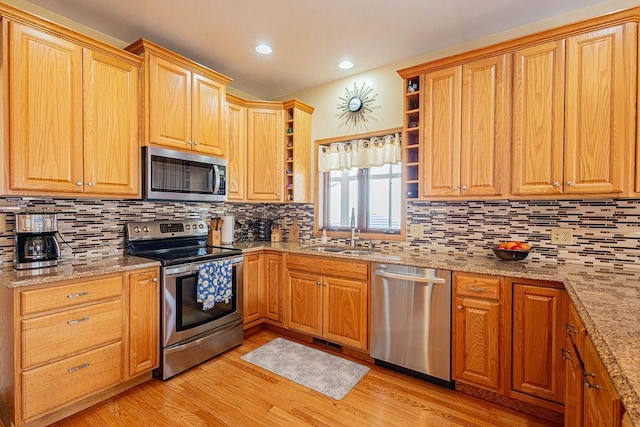 kitchen featuring light wood finished floors, a sink, light stone countertops, stainless steel appliances, and open shelves