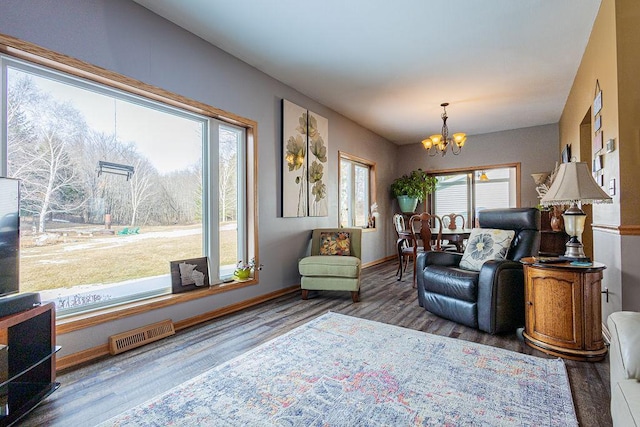 living area featuring a notable chandelier, wood finished floors, visible vents, and baseboards