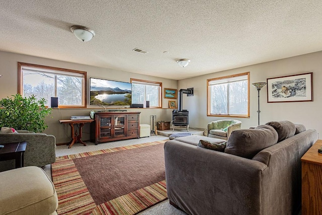 carpeted living area with visible vents, a textured ceiling, and a wood stove