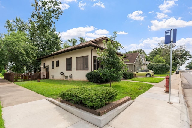 view of side of property featuring stucco siding, a lawn, and fence