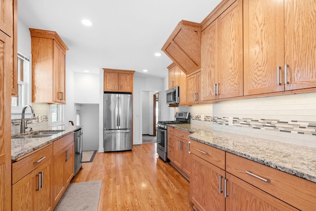 kitchen featuring light stone counters, light wood-style flooring, appliances with stainless steel finishes, and a sink