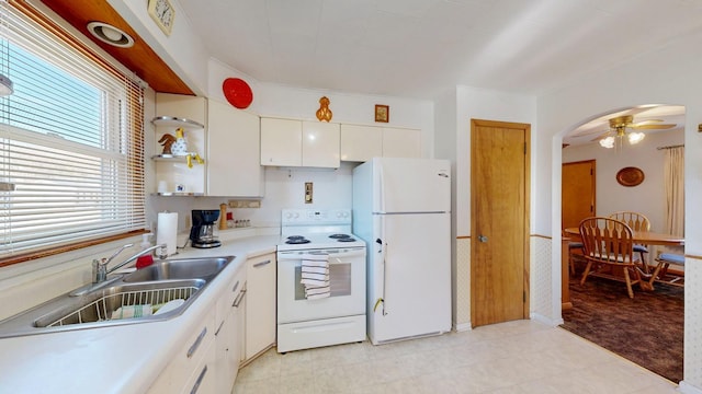 kitchen with light countertops, arched walkways, white cabinets, white appliances, and a sink