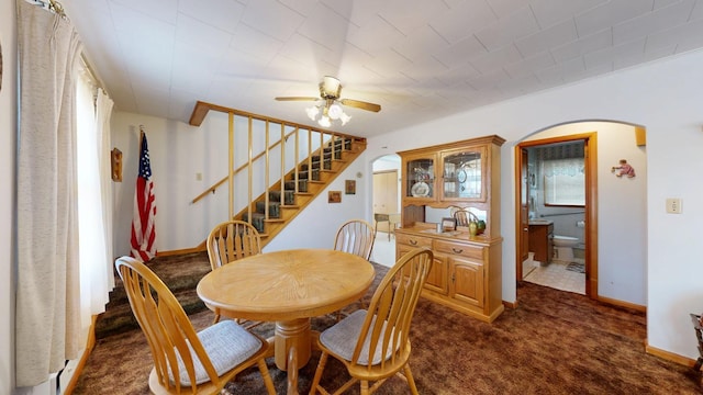 dining room featuring a ceiling fan, dark carpet, stairway, arched walkways, and baseboards