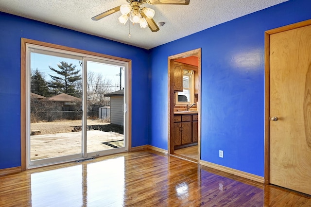 empty room featuring ceiling fan, baseboards, wood finished floors, a textured ceiling, and a sink