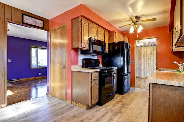 kitchen with ceiling fan, light countertops, light wood-style flooring, black appliances, and a sink