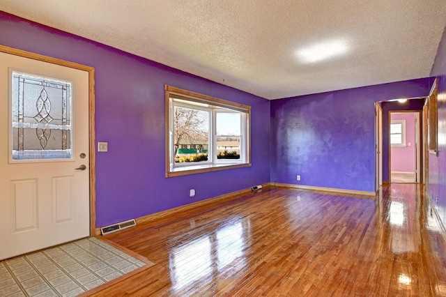 foyer featuring visible vents, a textured ceiling, baseboards, and wood finished floors