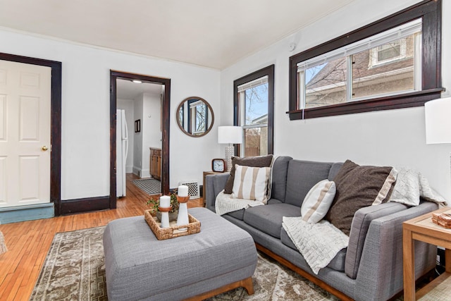 living area with visible vents, light wood-type flooring, baseboards, and ornamental molding