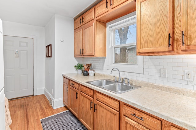 kitchen with baseboards, light countertops, decorative backsplash, light wood-style floors, and a sink