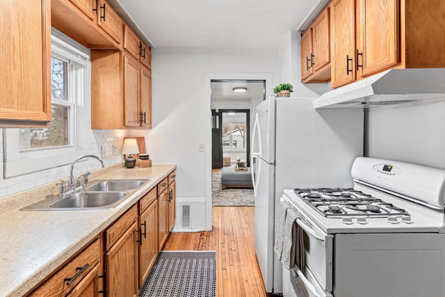 kitchen with white gas range, a sink, light countertops, light wood-style floors, and tasteful backsplash