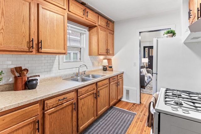 kitchen with light wood-type flooring, a sink, tasteful backsplash, white appliances, and light countertops