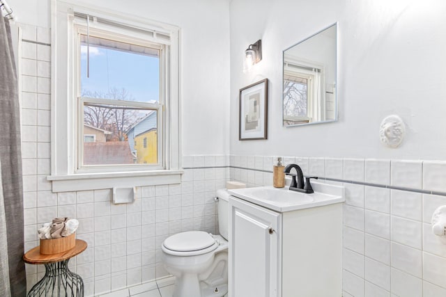 bathroom with toilet, tile walls, wainscoting, and vanity