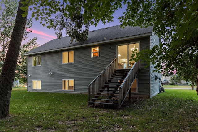 back of property with a yard, roof with shingles, and stairway