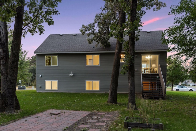 back of property at dusk featuring stairs, a garden, a yard, and roof with shingles