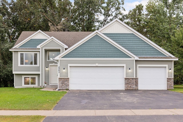 view of front facade featuring stone siding, a garage, driveway, and a front yard