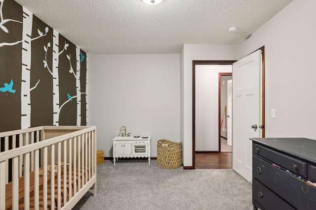 carpeted bedroom featuring a nursery area, baseboards, and a textured ceiling