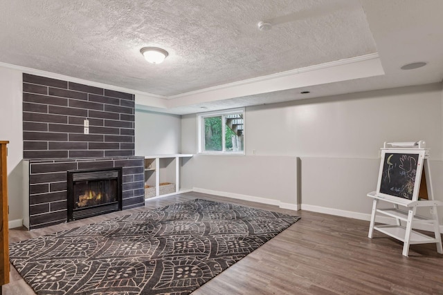 living area with a tiled fireplace, a textured ceiling, wood finished floors, crown molding, and baseboards