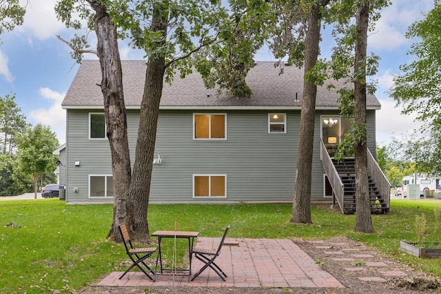 rear view of property with a yard, roof with shingles, stairs, and a patio area