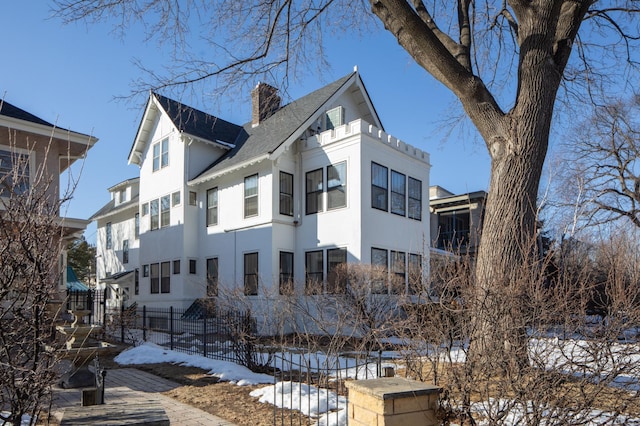 snow covered property featuring stucco siding, a chimney, and fence