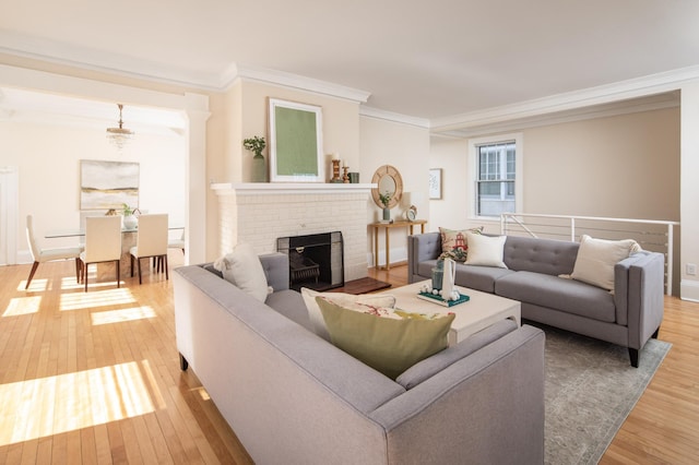 living room with crown molding, light wood-style flooring, a brick fireplace, and baseboards