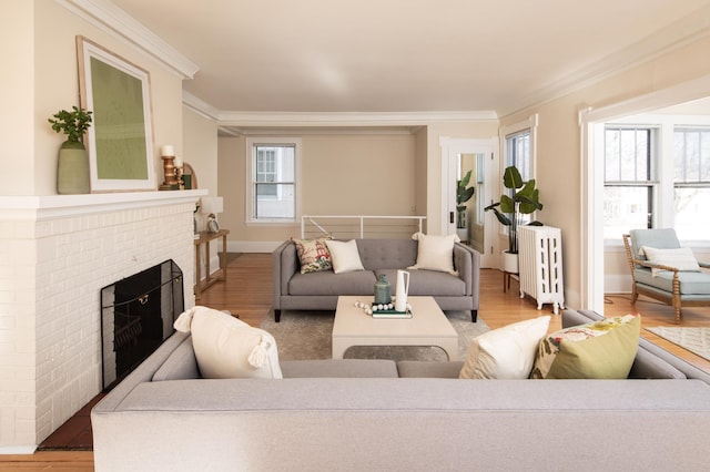 living room featuring radiator, a brick fireplace, crown molding, and light wood finished floors