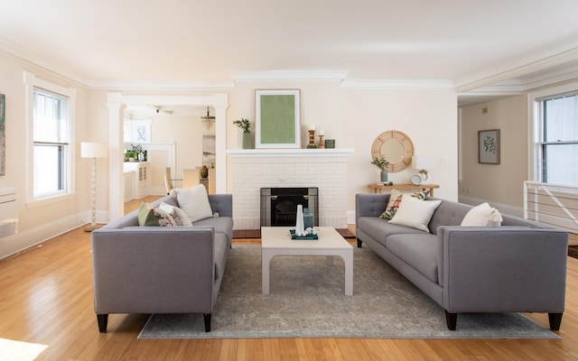 living room with baseboards, decorative columns, ornamental molding, a fireplace, and light wood-style floors