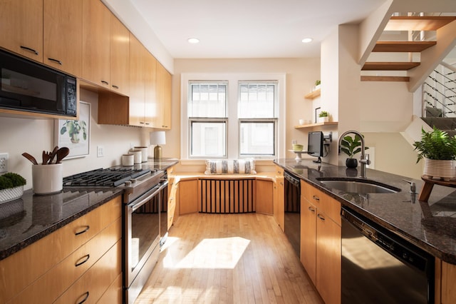 kitchen featuring a sink, dark stone counters, black appliances, and light wood-style flooring