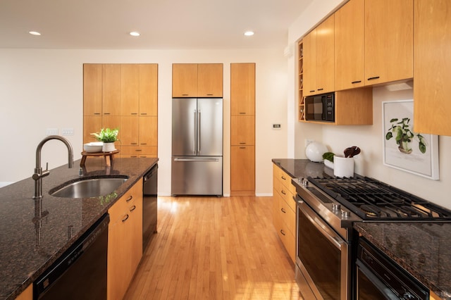 kitchen featuring dark stone counters, light wood-style flooring, recessed lighting, a sink, and black appliances