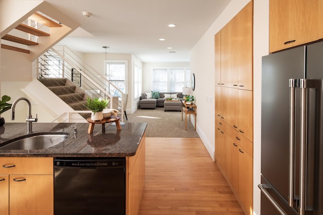 kitchen featuring a sink, recessed lighting, dark stone counters, high quality fridge, and dishwasher