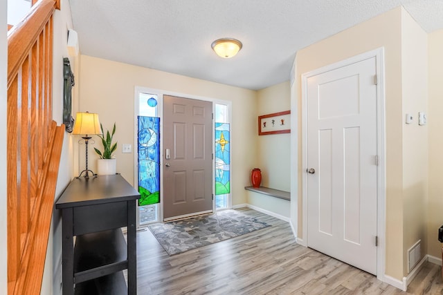 foyer featuring baseboards, light wood-style floors, visible vents, and a textured ceiling