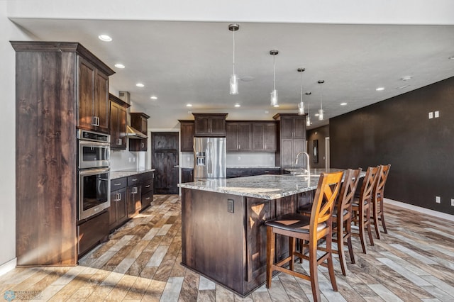 kitchen featuring recessed lighting, a large island with sink, stainless steel appliances, dark brown cabinets, and light wood-type flooring