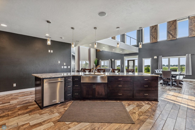 kitchen featuring a sink, open floor plan, dark brown cabinetry, light stone countertops, and hanging light fixtures