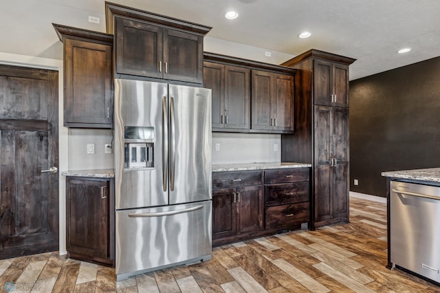 kitchen featuring dark brown cabinets, light stone countertops, light wood-style floors, and stainless steel appliances