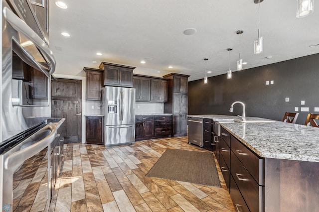 kitchen with pendant lighting, light stone counters, recessed lighting, dark brown cabinetry, and appliances with stainless steel finishes