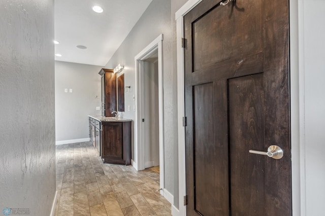 hall featuring recessed lighting, baseboards, a textured wall, and a sink