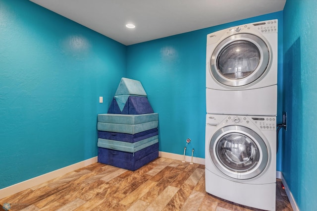 laundry room featuring baseboards, wood finished floors, laundry area, a textured wall, and stacked washer / drying machine