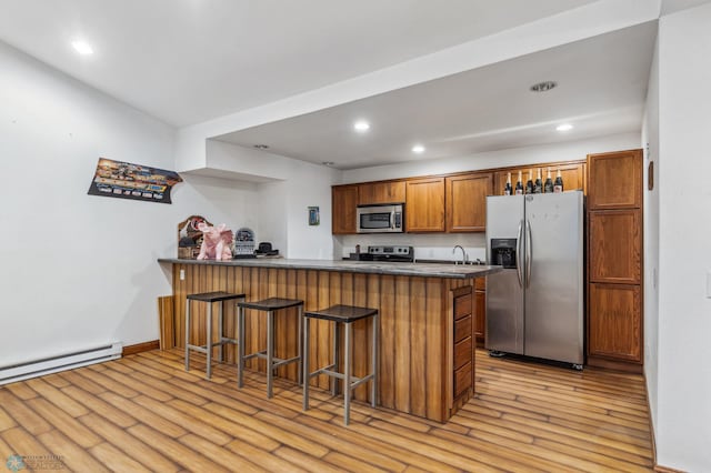 kitchen with a peninsula, dark countertops, light wood-type flooring, and stainless steel appliances