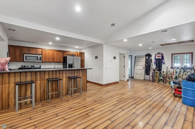 kitchen with light wood-type flooring, lofted ceiling, appliances with stainless steel finishes, dark countertops, and open floor plan