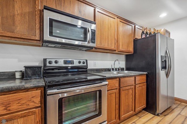 kitchen with light wood-style flooring, a sink, dark countertops, stainless steel appliances, and brown cabinetry