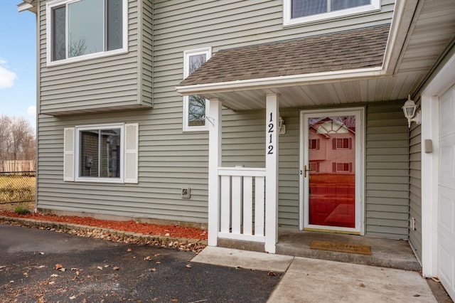 view of exterior entry with fence and a shingled roof