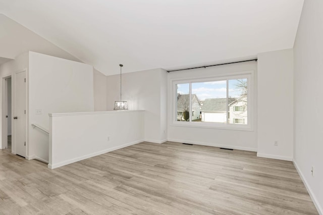 empty room featuring light wood-type flooring, visible vents, baseboards, lofted ceiling, and a chandelier