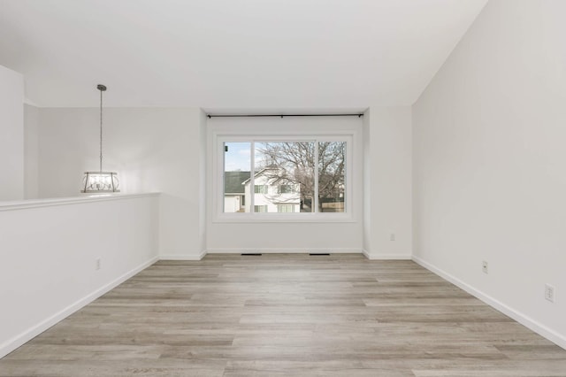 unfurnished room with light wood finished floors, a chandelier, and baseboards