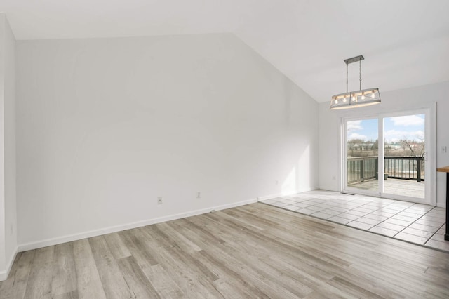 spare room featuring lofted ceiling, a notable chandelier, wood finished floors, and baseboards