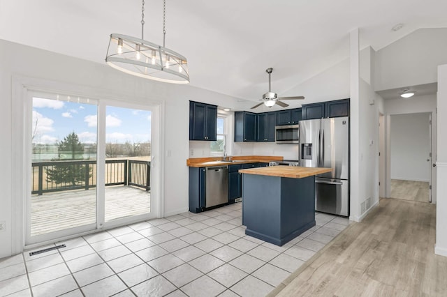 kitchen featuring blue cabinets, butcher block countertops, appliances with stainless steel finishes, and vaulted ceiling