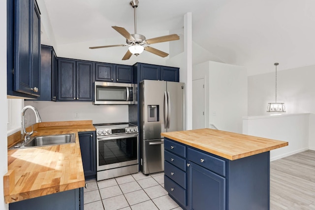 kitchen with a ceiling fan, a sink, stainless steel appliances, blue cabinets, and butcher block counters