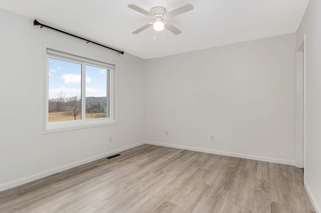 spare room featuring light wood finished floors, visible vents, baseboards, and ceiling fan